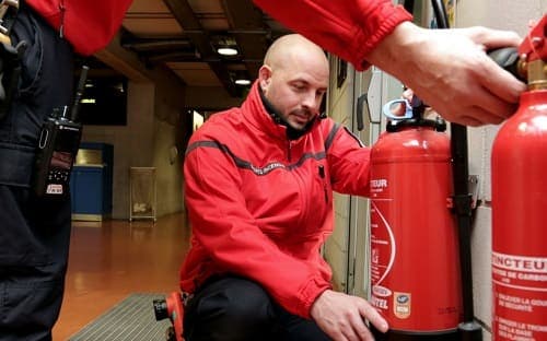 Agent Abis Security en veste rouge vérifiant des extincteurs, un collègue équipé d'une radio à ses côtés