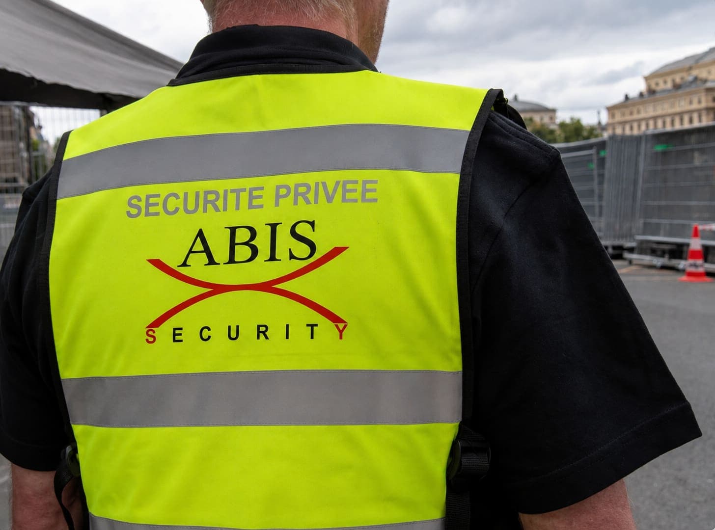 Agent Abis Security de dos, en gilet haute visibilité floqué Sécurité privée Abis Security, en poste devant des barrières